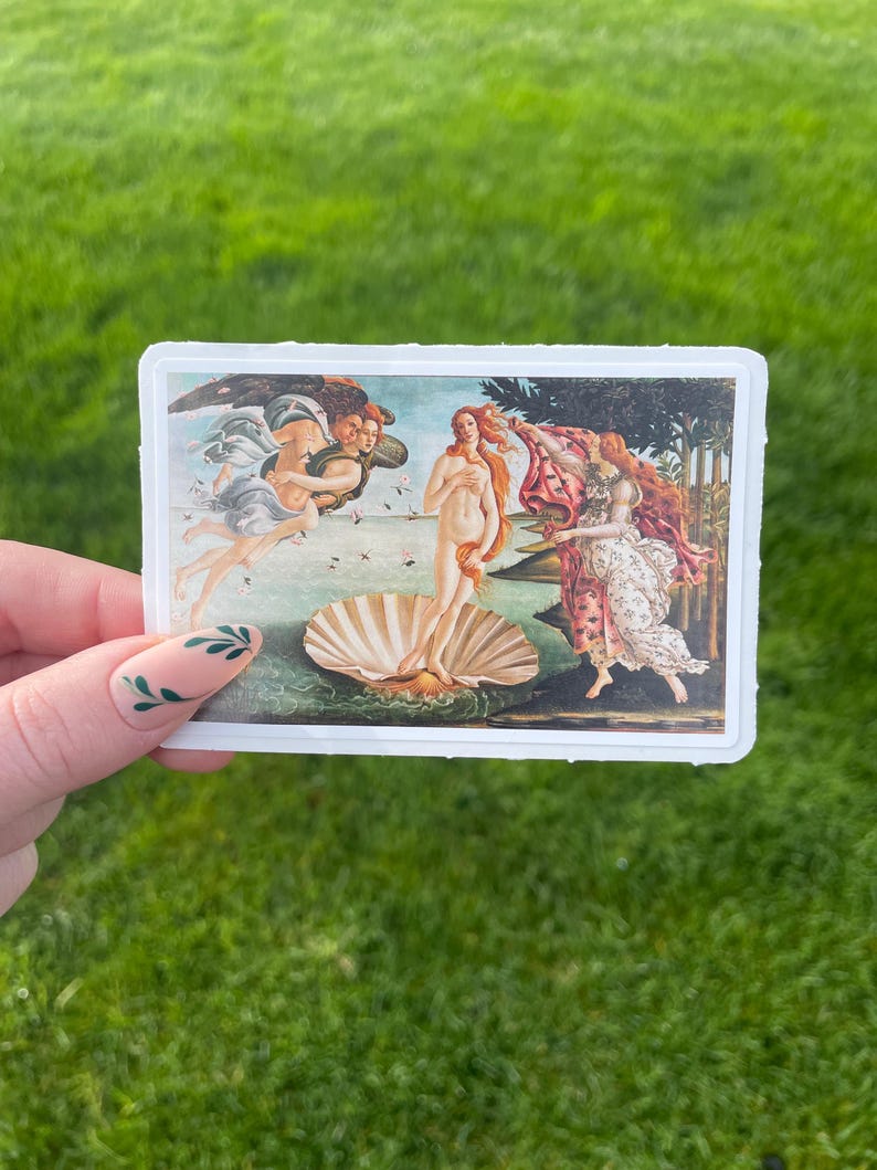 May include: A sticker featuring a reproduction of Sandro Botticelli's The Birth of Venus painting. The painting depicts a nude woman standing on a giant scallop shell, with the wind blowing her hair and a figure holding a cloak behind her.