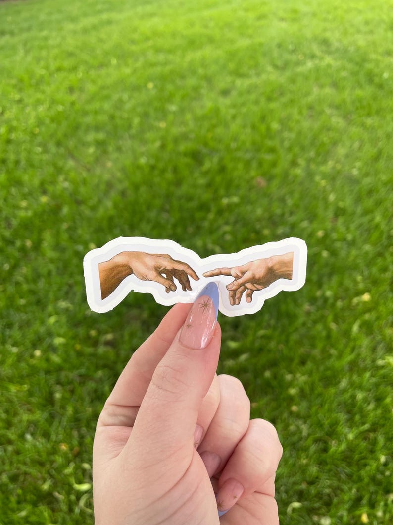 May include: A sticker featuring a depiction of the famous "Creation of Adam" painting by Michelangelo. The sticker shows two hands reaching towards each other, one from the left and one from the right, with a small gap between them.