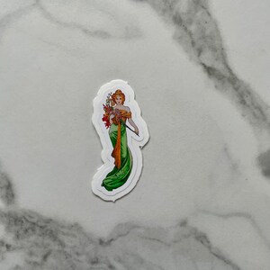 May include: A sticker featuring a woman in a green dress holding a bouquet of flowers. The woman has blonde hair and is wearing a crown of flowers.