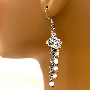 May include: Silver dangle earrings with a small, detailed charm and a chain of white beads.