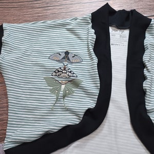 May include: A green and white striped cardigan with black trim and a butterfly design. The cardigan has a label that reads "Jami Saya" and "MED".