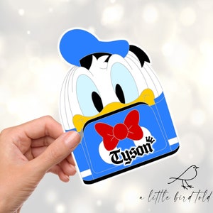 May include: A blue and white cartoon character with a red bow tie and the word "Tyson" printed on the front. The character is wearing a blue hat and has a yellow beak.