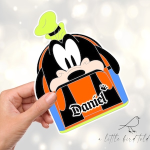 May include: Orange, black and blue Goofy character backpack with a yellow hat and the name "Daniel" printed on the front.