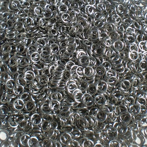 May include: A large pile of silver jump rings, a type of metal ring used in jewelry making.
