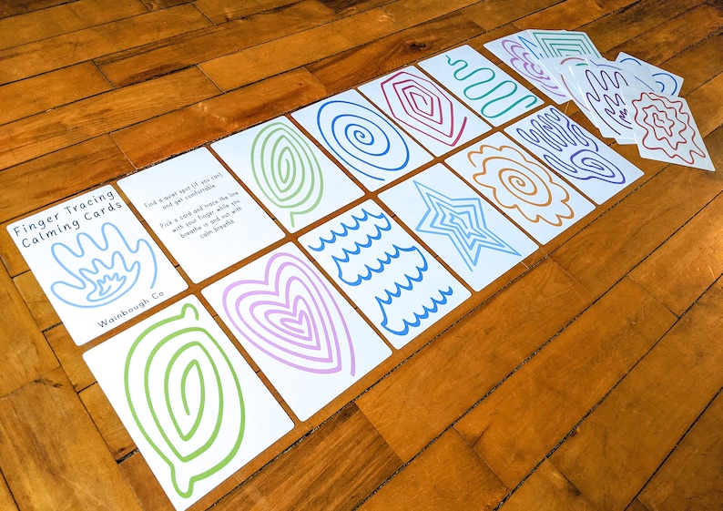 May include: A set of finger tracing calming cards with various shapes and patterns, including a heart, a star, waves, and spirals. The cards are white with colorful lines and the text "Finger Tracing Calming Cards" and "Wainbough Co."