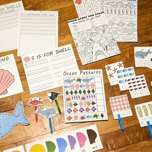 May include: A set of printable ocean-themed educational activities for children. The set includes a counting and colouring page, a pattern matching activity, a lacing activity, a writing activity, and a set of counting cards. The activities feature images of sea creatures such as whales, fish, seahorses, and seashells.