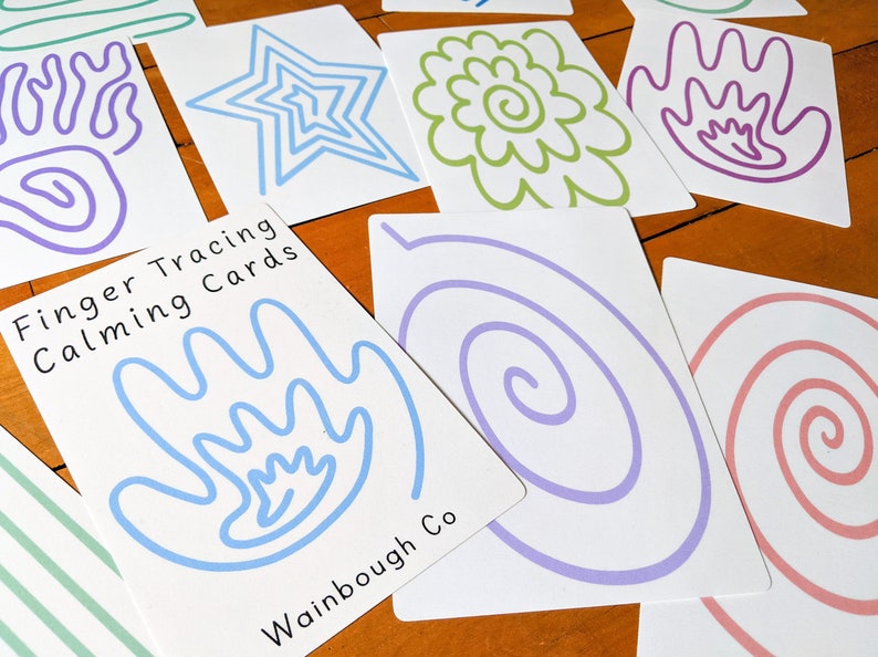 May include: Set of finger tracing cards with various shapes and designs, including a star, flower, spiral, and hand. The cards are white with blue, green, purple, and pink lines. The text on the cards reads "Finger Tracing Calming Cards" and "Wainbough Co."