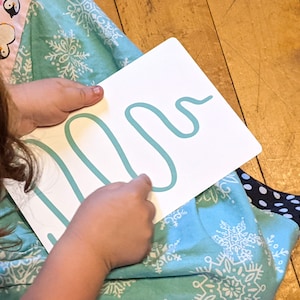 May include: A child traces a turquoise blue squiggly line on a white card with their finger.