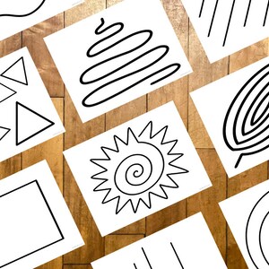 May include: A collection of white cards with black line drawings of various shapes and patterns, including triangles, rectangles, spirals, and wavy lines. The cards are arranged on a wooden surface.