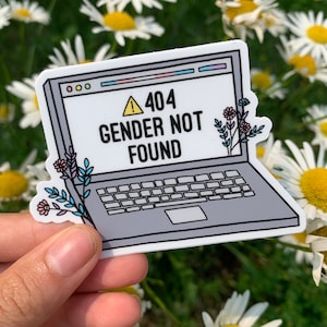 Può includere: Un adesivo per laptop bianco con una finestra del browser web blu e rosa. La finestra mostra un cartello di avvertimento giallo con un punto esclamativo e il testo "404 Genere non trovato". L'adesivo ha un design di laptop grigio con una tastiera e un touchpad bianco. Ci sono piccoli fiori viola, rosa e blu sul lato sinistro dell'adesivo.
