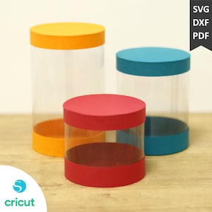 Può includere: Tre contenitori cilindrici trasparenti con coperchi e basi colorate. I coperchi e le basi sono arancioni, rossi e verde acqua. L'immagine include il testo "SVG, DXF, PDF" e il logo Cricut.
