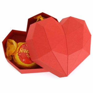 May include: A red heart-shaped box with a geometric design, open to reveal a yellow chocolate candy wrapped in gold foil. The candy has the text "Sereia de Ouro" printed on it.