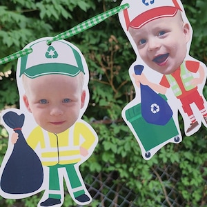 May include: Garbage truck driver garland with two cutouts. One cutout shows a smiling child in a green and white cap, yellow vest, and black trash bag. The other shows a child in a red and white cap, orange vest, and green trash can.