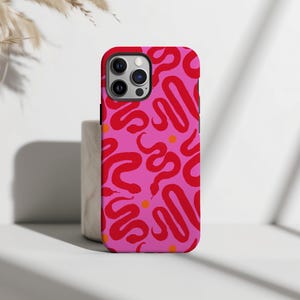 Op de afbeelding: Een smartphonehoesje met een felroze achtergrond en een herhalend patroon van rode, kronkelende slangensilhouetten en kleine, effen oranje cirkelvormige stippen verspreid over het ontwerp, inclusief een uitsparing voor de camera aan de linkerbovenkant.
