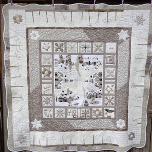 Könnte beinhalten: Eine weiße und beigefarbene Steppdecke mit einem quadratischen Design in der Mitte. Die Steppdecke besteht aus verschiedenen geometrischen Formen und Mustern, darunter Sterne, Schneeflocken und Blumen. Die Steppdecke ist mit einem weißen Rand eingefasst.