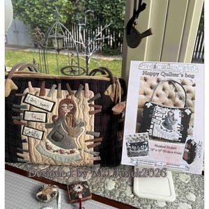 Op de afbeelding: Een handgemaakte, gewatteerde draagtas met een grillig ontwerp met een vrouw met naai-attributen en de tekst "I am born to craft". De tas is bruin en beige, met bijpassende handvatten. Een patroonvel wordt ernaast weergegeven.