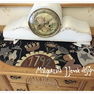 Può includere: Un orologio da camino bianco con un design floreale sul quadrante è posto su una credenza in legno con un runner trapuntato nero e marrone che presenta l'anno 1792 e il testo "Małgorzata J.Jevek design".