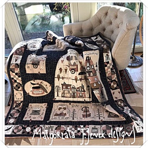 Può includere: Una trapunta nera e crema con un design a patchwork che presenta varie scene di una piccola città. La trapunta è piegata e drappeggiata su una poltrona color crema. La trapunta è firmata "Malgorzata J. Jędrzejczyk Designs".