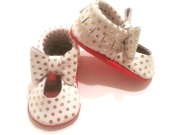 Mocasines Mary Jane de cuero hechos a mano, blancos con lunares dorados y suela roja.