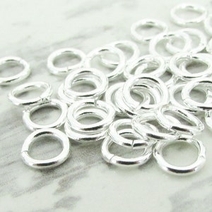 May include: A pile of silver jump rings, a type of jewellery finding used for connecting chains, cords, and other jewellery components.