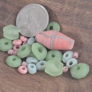 May include: A collection of colorful beads in various shapes and sizes, including green donut-shaped beads, pink round beads, and a large pink bead with a striped design. A US quarter coin is also present.