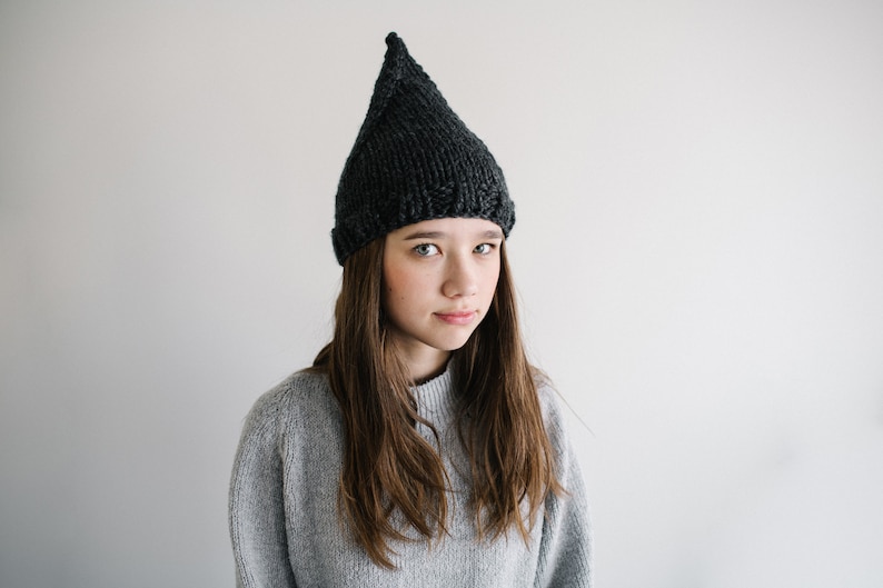 May include: A person wearing a gray sweater and a black knit hat with a pointed top.