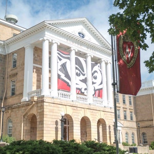 May include: A large, tan stone building with white columns and a red banner with a white logo. The banner reads "Badger Hall".