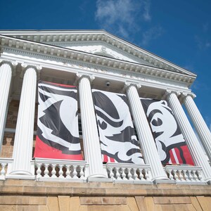 May include: A white building with columns and a red, black, and white banner with a badger mascot. The banner reads "Wisconsin Badgers".