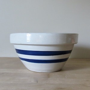 May include: A white ceramic mixing bowl with two blue stripes around the middle.