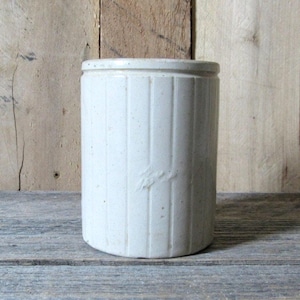 May include: White ceramic jar with vertical lines and a subtle speckled texture. The jar has a simple, cylindrical shape.