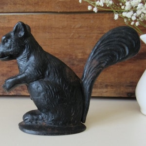 May include: A black cast iron squirrel nutcracker. The squirrel is sitting upright with its tail curled behind it.
