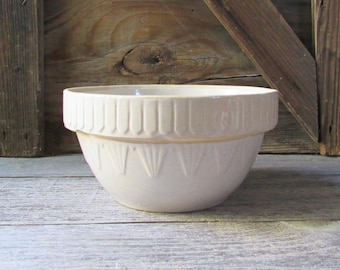 May include: A cream-colored ceramic mixing bowl featuring a wide, reinforced rim with vertical indentations and a lower section decorated with a repeating fan-shaped embossed pattern around the exterior circumference of the vessel.
