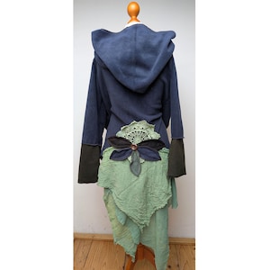 Può includere: Una giacca con cappuccio blu navy con maniche lunghe grigio scuro e un pannello in tessuto verde chiaro testurizzato sull'orlo. Il retro è decorato con un centrino all'uncinetto verde chiaro e un fiore in tessuto blu navy con un bottone marrone.