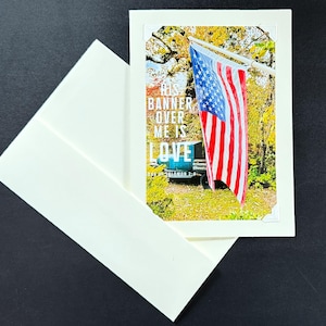 May include: A card with a photo of an American flag waving in the wind. The text on the card reads "His banner over me is love."  The card is on a white envelope.