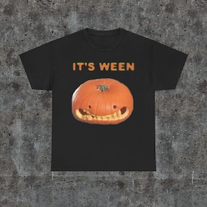 Puede incluir: Camiseta negra con el texto "IT'S WEEN" y una calabaza tallada con una sonrisa de dientes.
