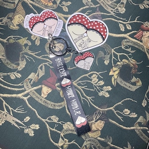 May include: A black keychain with a red and white heart-shaped charm. The charm features a graphic of a woman's backside with a red and white polka dot pattern. The keychain also has a black ribbon with the text "Bad Intentions" and "Moot Noodle" printed on it.
