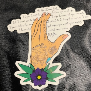 May include: A sticker of a hand with a skull and flower tattoo. The hand is holding a note that reads "To the Dark Lord, I know I will be... before you read this I who discovered your secret. And intend to destroy it as soon as I can. That when you meet your match, mortal once more. R.A.B."