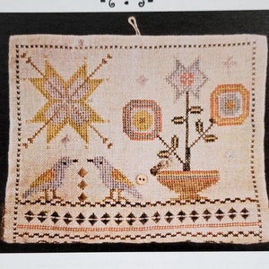 May include: A cross-stitch pattern featuring a floral design with two birds, a star, and a small button. The pattern is titled "Birdy Stitching Roll" and is designed by Lori Markovic. The text "La-D-Da designs for counted thread" is also included.