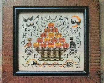 May include: A cross-stitch pattern for a Halloween-themed design featuring a basket of pumpkins, bats, and a black cat. The pattern is titled "October 31st" and is by Kathy Barrick.