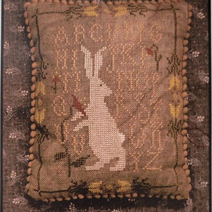 May include: Cross stitch pattern featuring a white rabbit with long ears, surrounded by flowers and leaves. The pattern is titled "Briar Rabbit" and is from La-D-Da designs for counted thread.