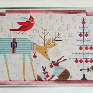 May include: Cross stitch pattern featuring a deer wearing pajamas, two bunnies wearing pajamas, a cardinal, and a Christmas tree with red ornaments. The pattern includes the alphabet and the text "Kind & Gentle Woodland Holiday Sampler".