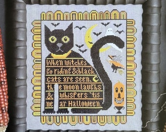 May include: A framed cross-stitch pattern featuring a black cat with a yellow collar and the text 'Tis Near Halloween. When witches so riding & black cats are seen. The moon laughs & whispers 'tis near Halloween.' by Kathy Barrick.