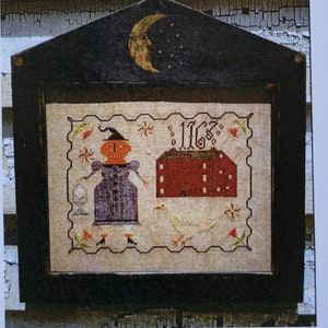 May include: A cross-stitch pattern featuring a witch, a house, and a goose. The pattern is framed in a black frame with a crescent moon and stars painted on the top. The text "Notforgotten Farm 1887" and "Prunella Squashbottom" are printed on the page. The stitch count is 144W x 114h and the finished project is approximately 10 inches by 8 inches.