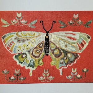 Puede incluir: Un patrón de punto de cruz contado que presenta una mariposa colorida con acentos florales sobre un fondo rojo. El patrón se titula "A Study in Nature" y es de The Artsy Housewife.