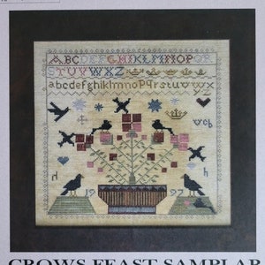 May include: A cross-stitch sampler pattern featuring a stylized tree with crows perched on branches. The tree is in a pot and surrounded by flowers. The sampler includes the alphabet and the text "Crows Feast Sampler".