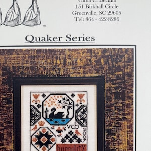 May include: A framed cross-stitch sampler from the "Quaker Series" featuring a central design with a swan, stars, and the word "humility." The frame has a dark, textured appearance. The image includes the text "Examplar Dames Design Co."