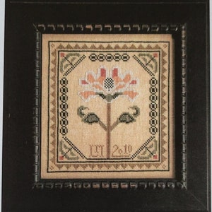 May include: A framed cross-stitch design featuring a stylized flower in shades of peach, orange, and green. The design is set against a beige background and framed in black. The text "Sarah Lowell" and "La-D-Da designs for counted thread" are also visible.