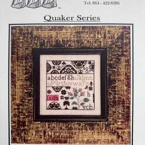 May include: A framed cross-stitch sampler with the word "Faith" in a pink box. The sampler features an alphabet, floral motifs, and the text "Quaker Series". The frame has a textured, gold-toned finish.