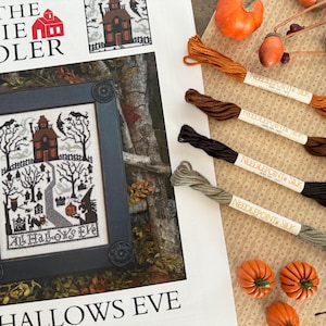 May include: A framed cross-stitch pattern with a Halloween theme, featuring a haunted house, trees, and a path. The text "All Hallows Eve" is visible.  Four spools of needlepoint silk thread in shades of brown, black, and green are also present.