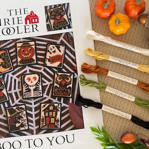 May include: A Halloween-themed cross-stitch pattern book with various designs, including a black cat, pumpkin, ghost, and owl. The image also features colorful embroidery floss and decorative gourds.